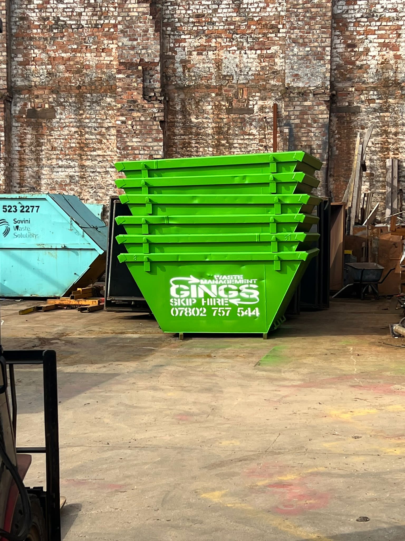 A stack of green Gings skips in a yard beside a brick wall