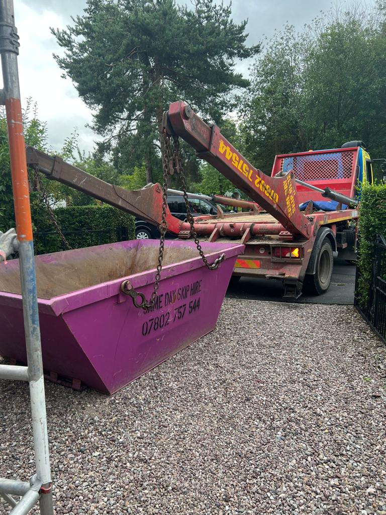 A purple Same Day Skip Hire skip on a gravel drive as the lorry lifts away